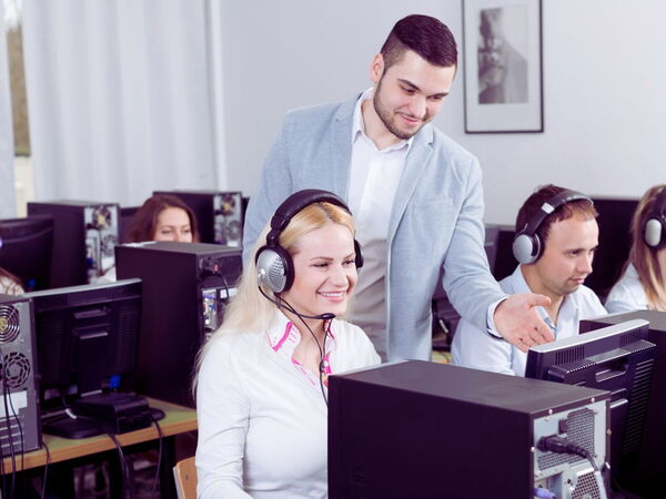 Supervisor, der die Agenten in einem modernen Callcenter mit Computern und einem auf Kundenservice ausgerichteten Unternehmensumfeld anleitet.